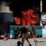 A police officer retrives items in front of a police checkpost burned by protesters near the US Consulate General