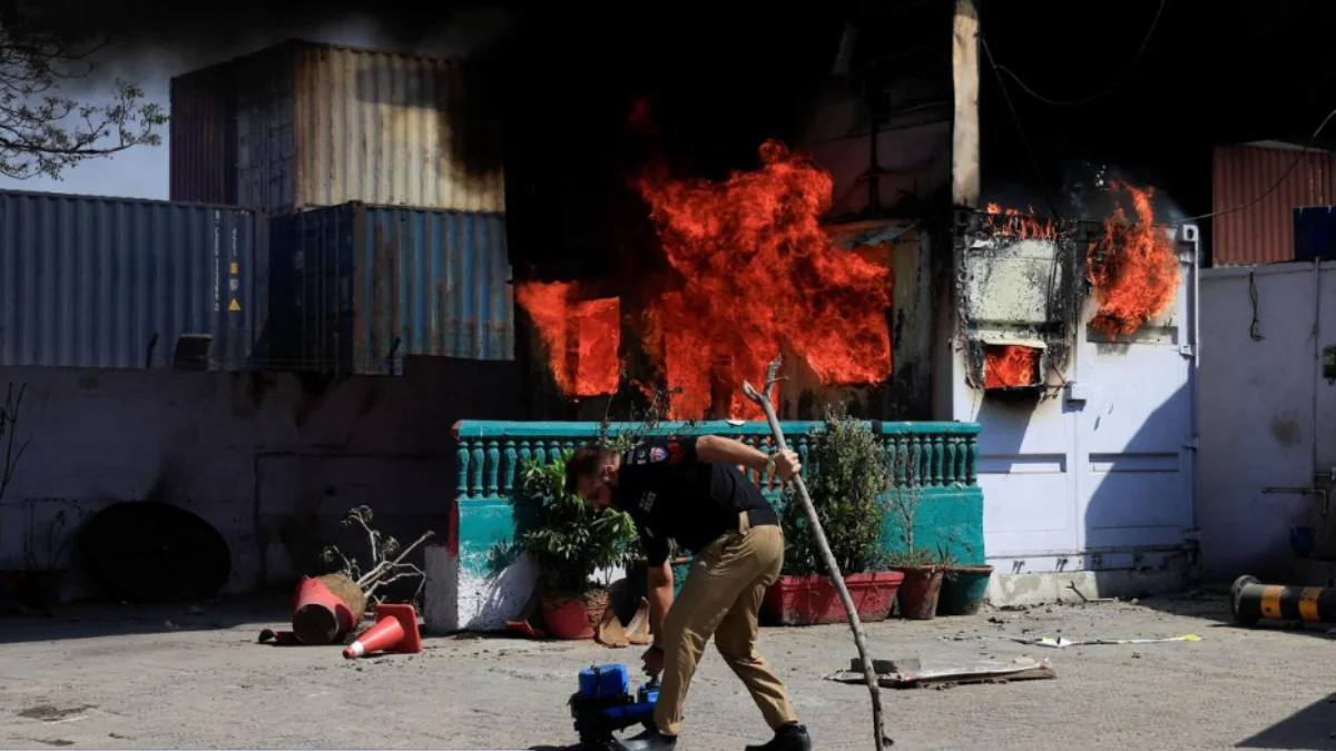 A police officer retrives items in front of a police checkpost burned by protesters near the US Consulate General